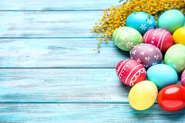 Colorful easter eggs with yellow flowers on blue wooden table — Stock Photo, Image