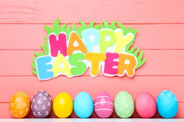 Huevos coloridos con texto Feliz Pascua sobre fondo de madera — Foto de Stock