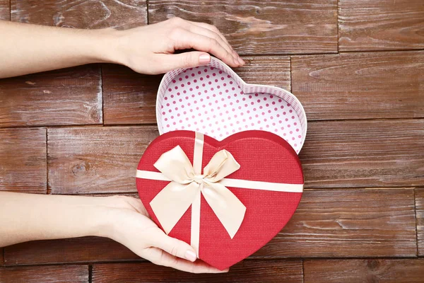 Mains féminines ouvrant boîte cadeau en forme de coeur sur table en bois — Photo