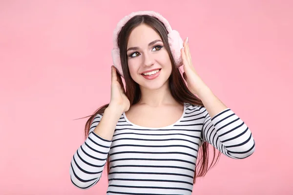 Mooie jonge vrouw met warme koptelefoon op roze achtergrond — Stockfoto