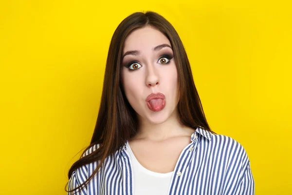 黄色の背景に舌を見せて美しい若い女性 — ストック写真