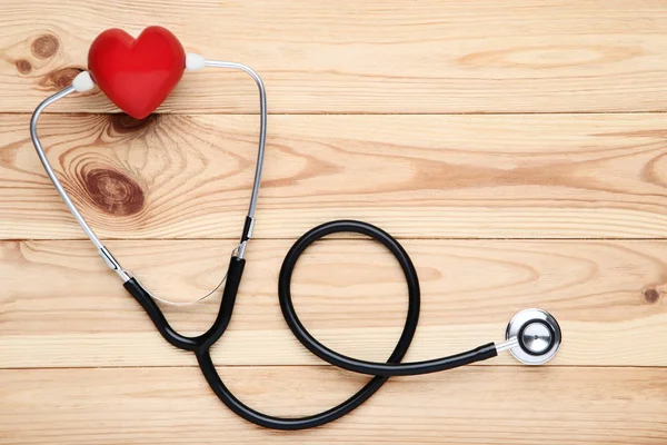 Stetoskop s červeným srdcem na hnědém dřevěném stole — Stock fotografie