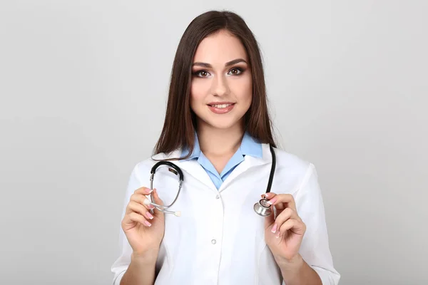 Retrato de jovem médico com estetoscópio sobre fundo cinza — Fotografia de Stock