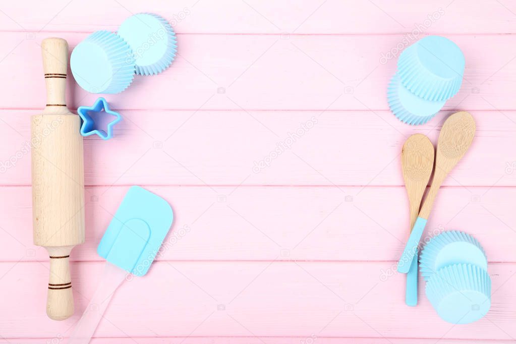 Cupcake cases with kitchen utensils on pink wooden table