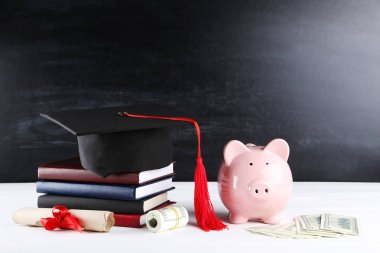 Mezuniyet kapağı, para ve tahta üzerine kitap ile piggybank ba