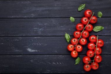 Siyah ahşap masada fesleğen yapraklarla kiraz domates