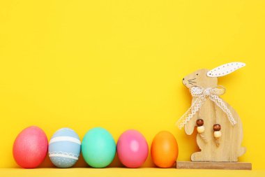 Sarı arka planda ahşap tavşan ile renkli Paskalya yumurtası