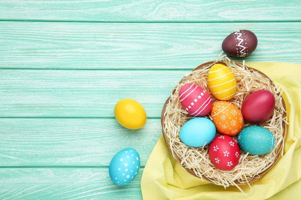 Colorate uova di Pasqua nel cestino con tovagliolo sul tavolo di legno — Foto Stock