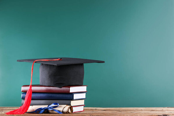 Graduation cap with diploma and stack of books on green board ba