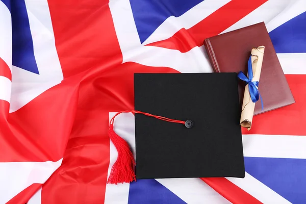 Tapa de graduación con diploma y bloc de notas en fondos de bandera británica —  Fotos de Stock