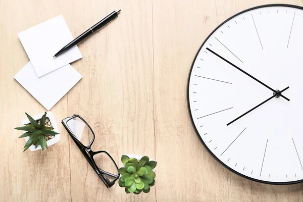 Round clock with green plants, glasses and papers on brown woode — Stock Photo, Image