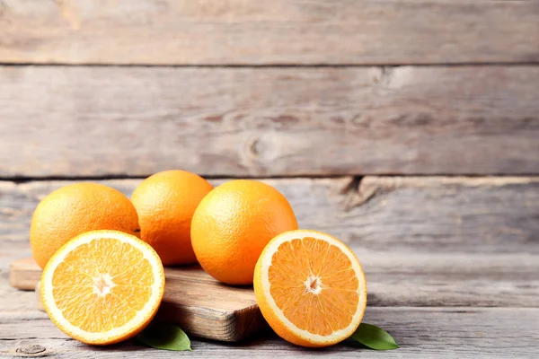 Frutas de laranja com folhas verdes e tábua de corte em t de madeira cinza — Fotografia de Stock