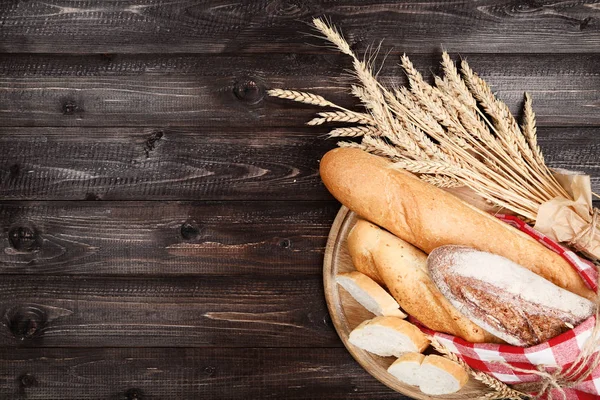 Baguettes frescos con espigas de trigo sobre mesa de madera marrón — Foto de Stock