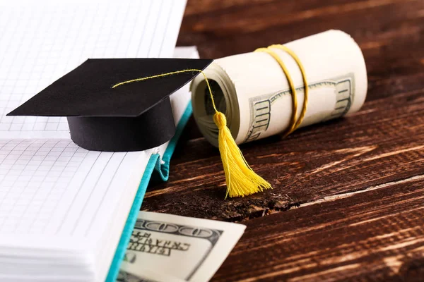 Small graduation cap with dollar banknotes and notepad on brown — Stock Photo, Image