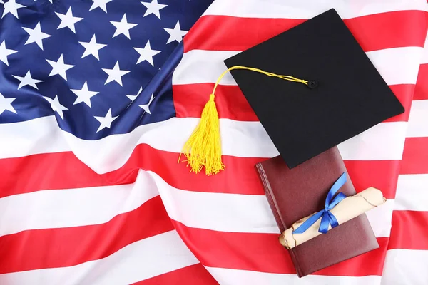 Graduation cap with diploma and notepad on American flag backgro