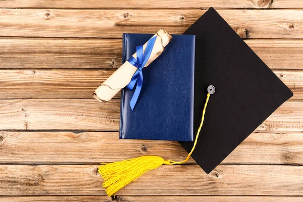 Graduation cap with diploma and book on brown wooden table