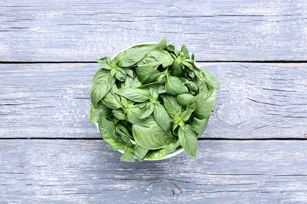 Green basil leafs in bowl on grey wooden table — Stock Photo, Image