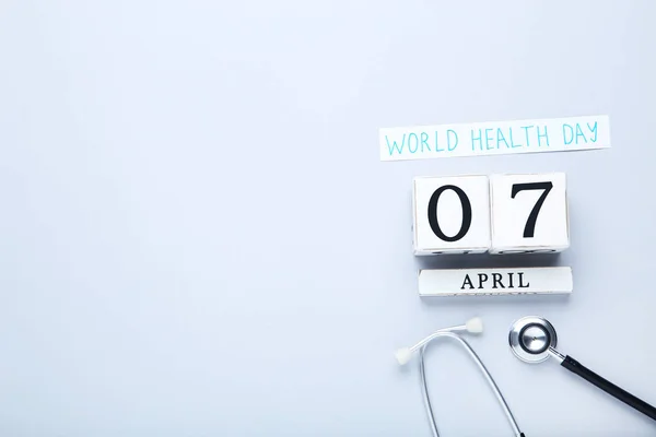 Text World Health Day with stethoscope and cube calendar on grey