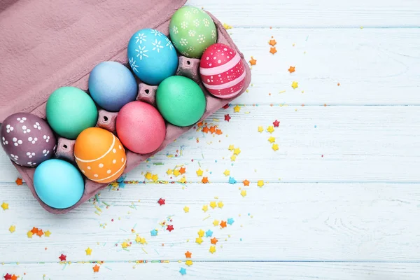 Uova di Pasqua colorate in scatola di cartone con spruzzi su tavola di legno — Foto Stock