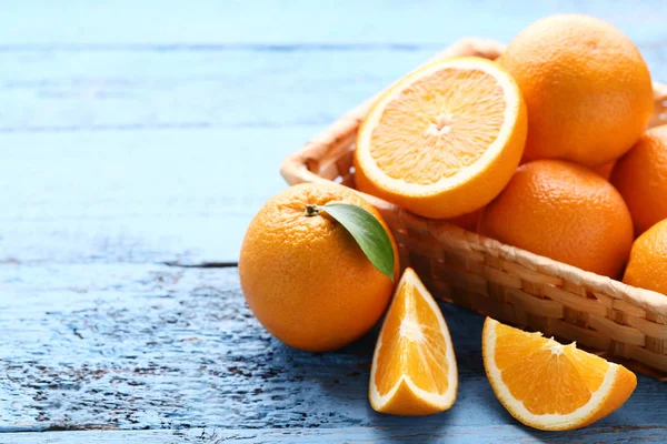 Fruta naranja con hoja verde y cesta sobre mesa de madera azul —  Fotos de Stock