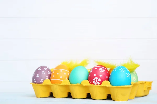 Colorful easter eggs in carton box on wooden table — Stock Photo, Image