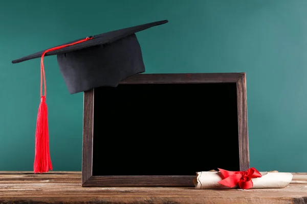 Tapa de graduación con diploma y marco en blanco en respaldo de tablero verde — Foto de Stock
