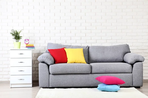 Weißer Nachttisch neben grauem Sofa mit bunten Kissen auf Zierleisten — Stockfoto