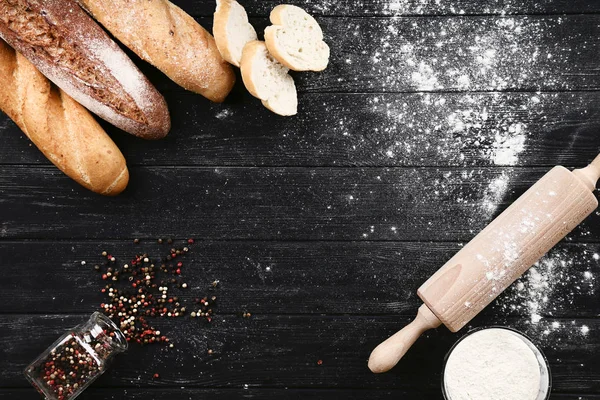 Baguettes fraîches avec assaisonnement au poivre et farine sur bois noir — Photo