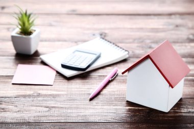 Hesap makinesi ve kahverengi ahşap masa üzerinde yeşil bitki ile ev modeli