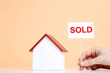 Ahşap ev modeli ve kağıt ile bej renkli arka plan üzerinde metin satıldı