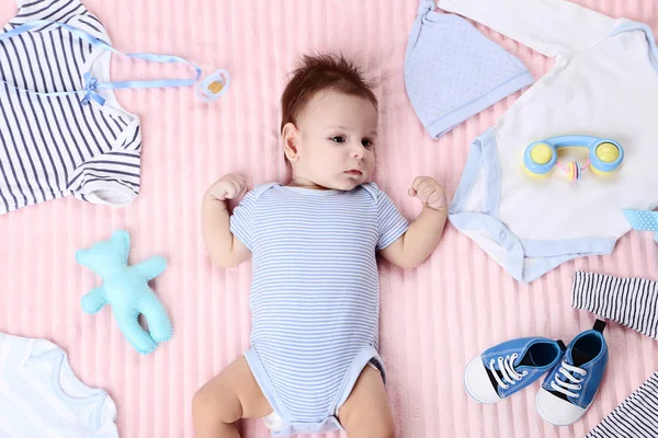 Bebê bonito com roupas de moda e brinquedos deitados na cama rosa — Fotografia de Stock