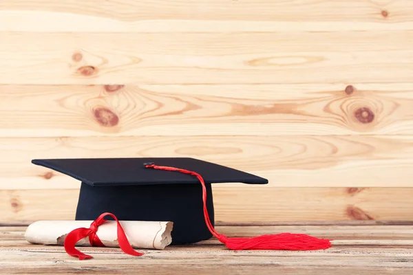 Graduation cap with diploma on brown wooden table — Stock Photo, Image