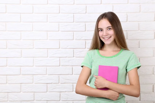 Jeune fille avec livre sur fond de mur de briques blanches — Photo
