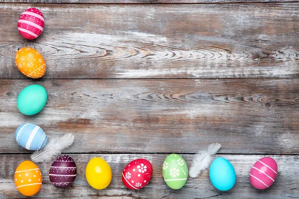 Ovos de páscoa coloridos com penas na mesa de madeira marrom — Fotografia de Stock