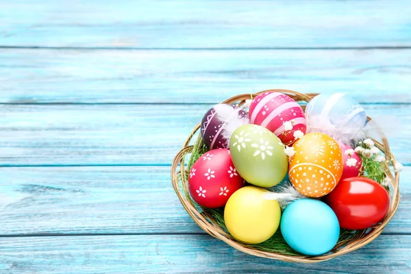 Oeufs de Pâques colorés dans le panier avec des fleurs de gypsophila sur bois — Photo