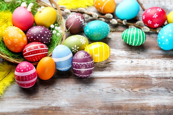 Œufs de Pâques colorés avec des plumes et des fleurs sur une table en bois — Photo