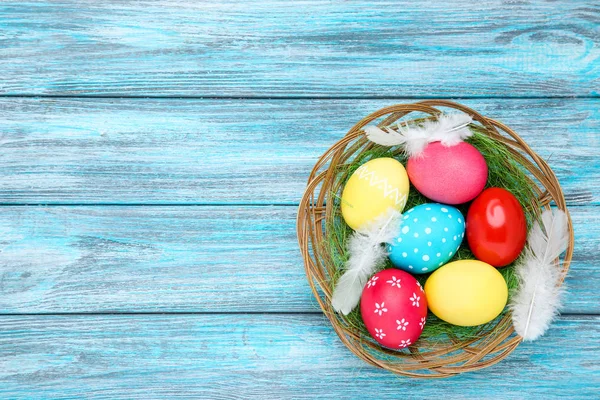 Ovos de páscoa coloridos em cesta com penas brancas em woode azul — Fotografia de Stock