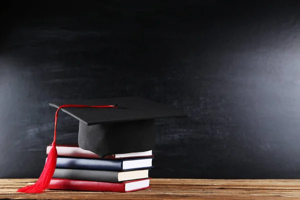 Tapa de graduación con pila de libros sobre fondo de pizarra — Foto de Stock