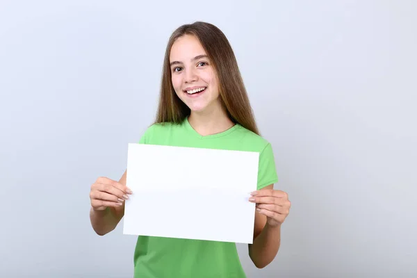 Menina segurando folha de papel em branco no fundo cinza — Fotografia de Stock