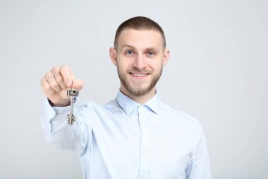Young man with silver keys on grey background