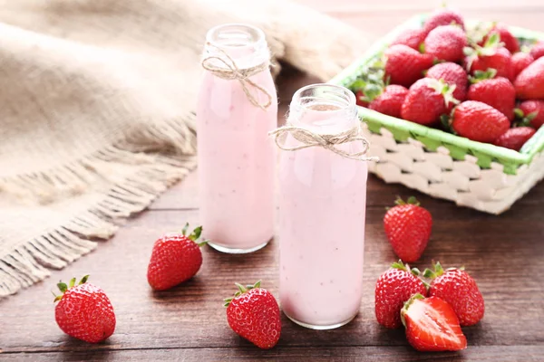 Smoothie w szklanych butelkach z truskawkami na brązowym drewnianym tablu — Zdjęcie stockowe