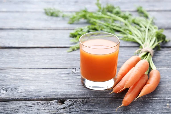 Свежая морковь со стаканом сока на сером деревянном столе — стоковое фото