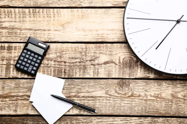 Okrągły zegar z kalkulatorem, długopisem i arkuszem papieru na brązowym wo — Zdjęcie stockowe