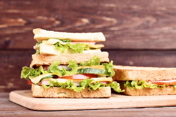 茶色の木製の背景にまな板とおいしいサンドイッチ — ストック写真