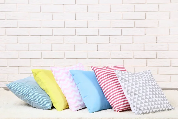 Travesseiros coloridos macios no fundo da parede de tijolo — Fotografia de Stock