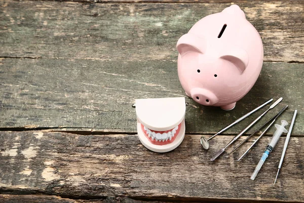 Gri ahşap üzerinde diş modeli ve tıbbi araçlar ile pembe kumbara — Stok fotoğraf