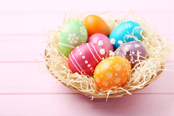 Barevná velikonoční vejce v koši na růžovém dřevěném stole — Stock fotografie