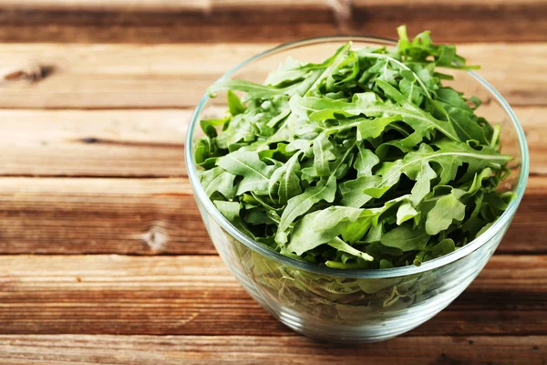 Folhas de arugula verde em tigela de vidro na mesa de madeira marrom — Fotografia de Stock