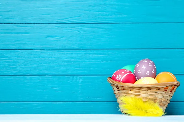 Œufs de Pâques colorés dans le panier avec plume jaune sur fond bleu — Photo