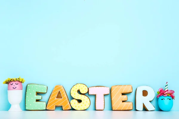 Cute eggs and word Easter by gingerbread cookies on blue backgro — Stock Photo, Image